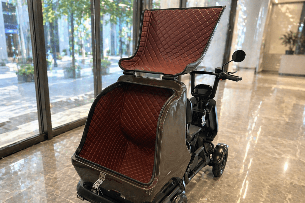 Brown quilted leather seat and open storage compartment on a mobility scooter inside a showroom with marble floor and glass walls in the background
