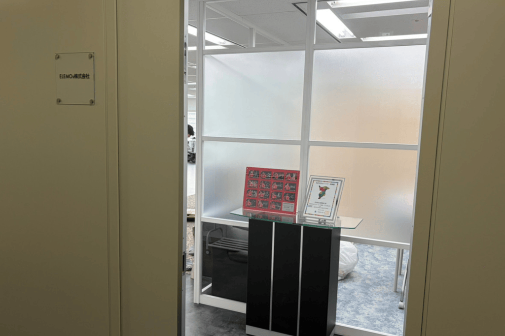Office entrance to a reception area with a glass display stand and framed posters on a glass-topped pedestal near frosted panels.