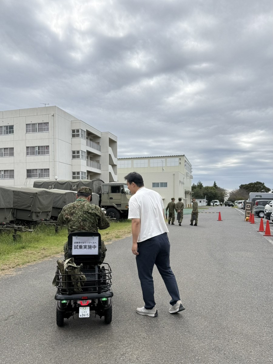 松戸駐屯地展示会でELEGRANに試乗する来場者と並走するELEMOsスタッフ